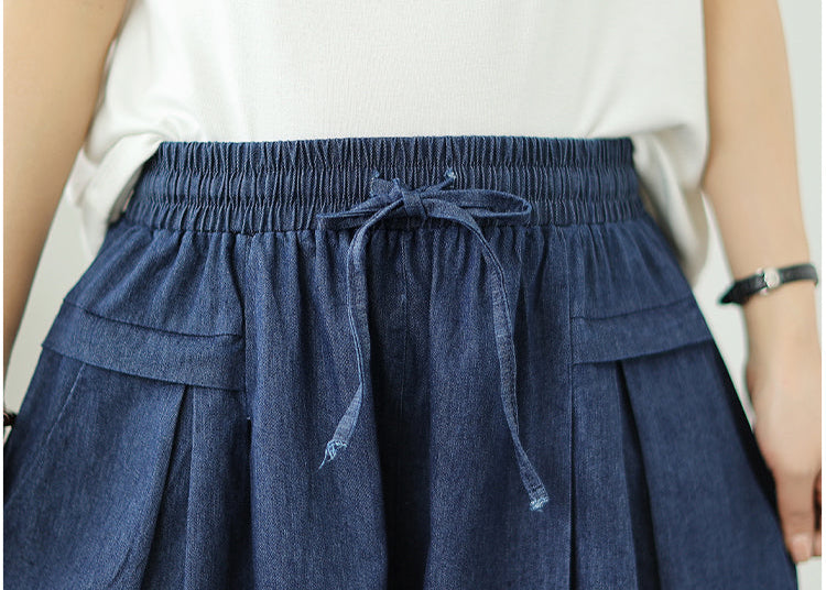 Navy blue denim skirt with a tie detail worn by a person, on a plain background.