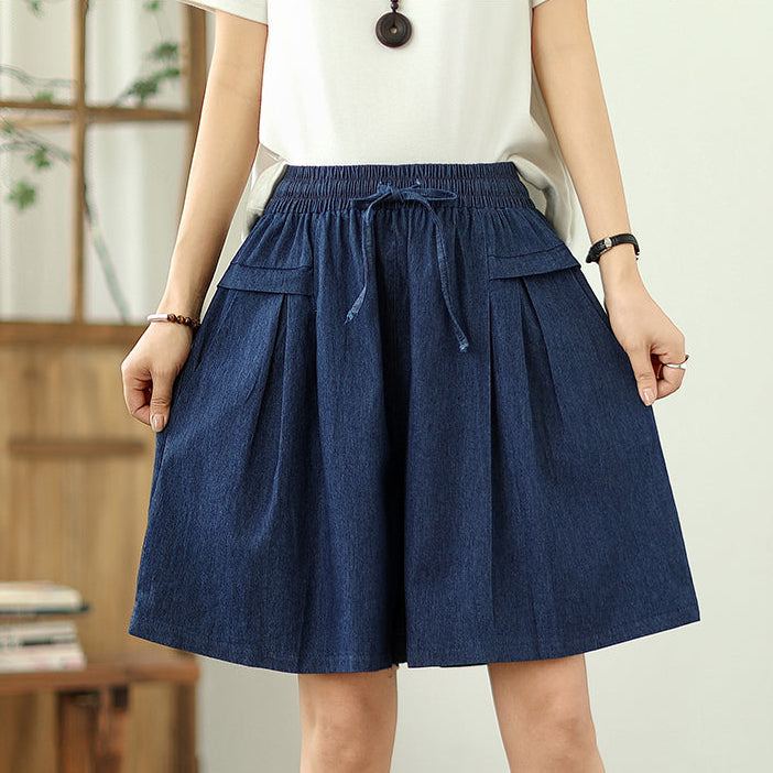 Person wearing a blue denim skirt with a white top against a neutral background