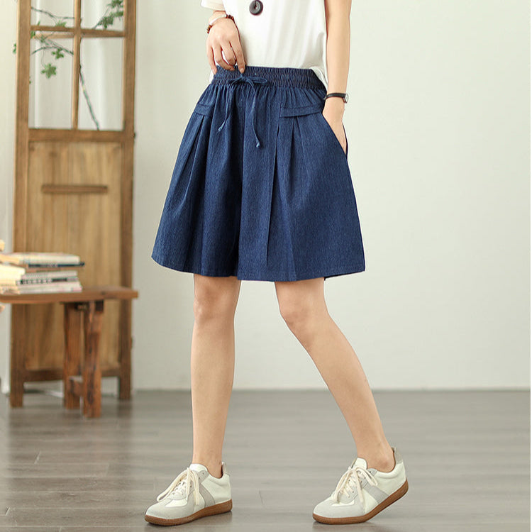 Person wearing a blue skirt and white sneakers in a minimal indoor setting