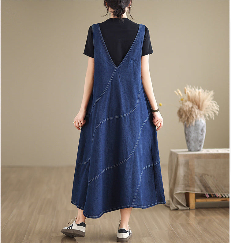 Person wearing a blue denim dress over a black top in a room with a table and vase.