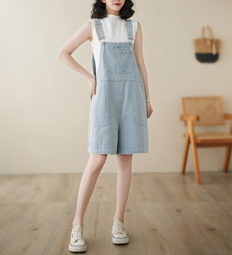 Woman wearing a light blue denim dress with a white shirt underneath, standing in a room with wooden flooring and a wooden chair.