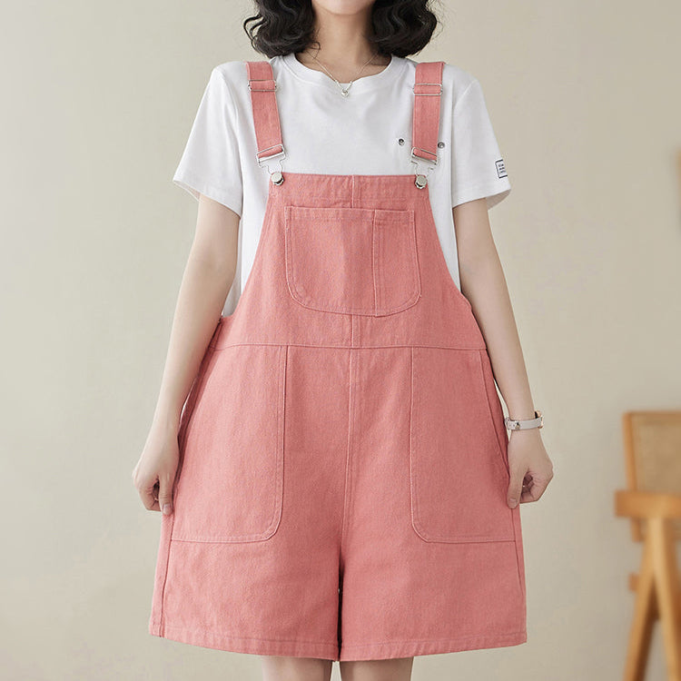 Person wearing a white t-shirt and pink denim overalls against a plain background