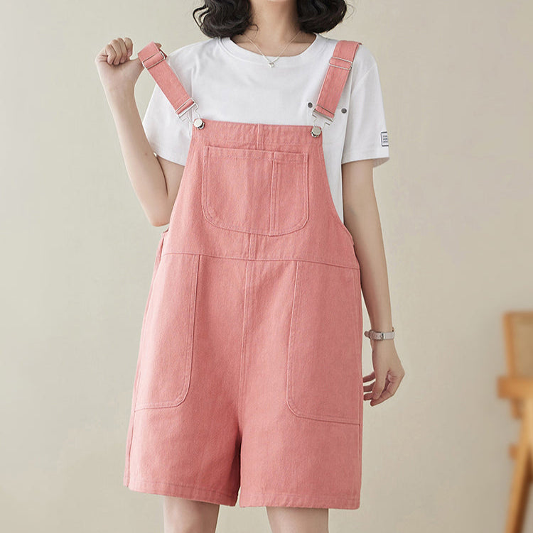 Person wearing a pink denim overalls with a white shirt on a plain background