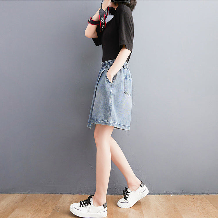 Person wearing a black top and denim skirt against a gray wall.