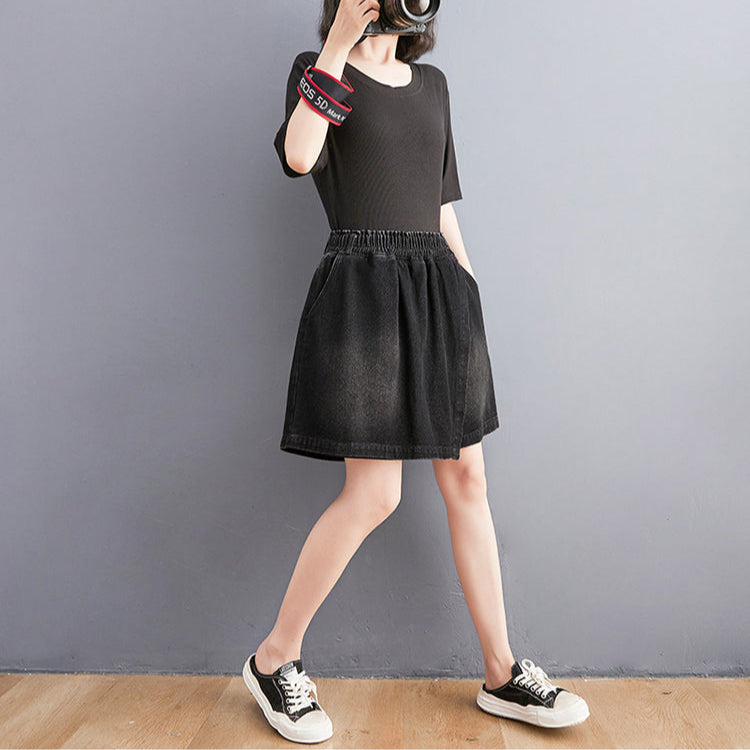 Person wearing a black dress and sneakers against a gray wall.