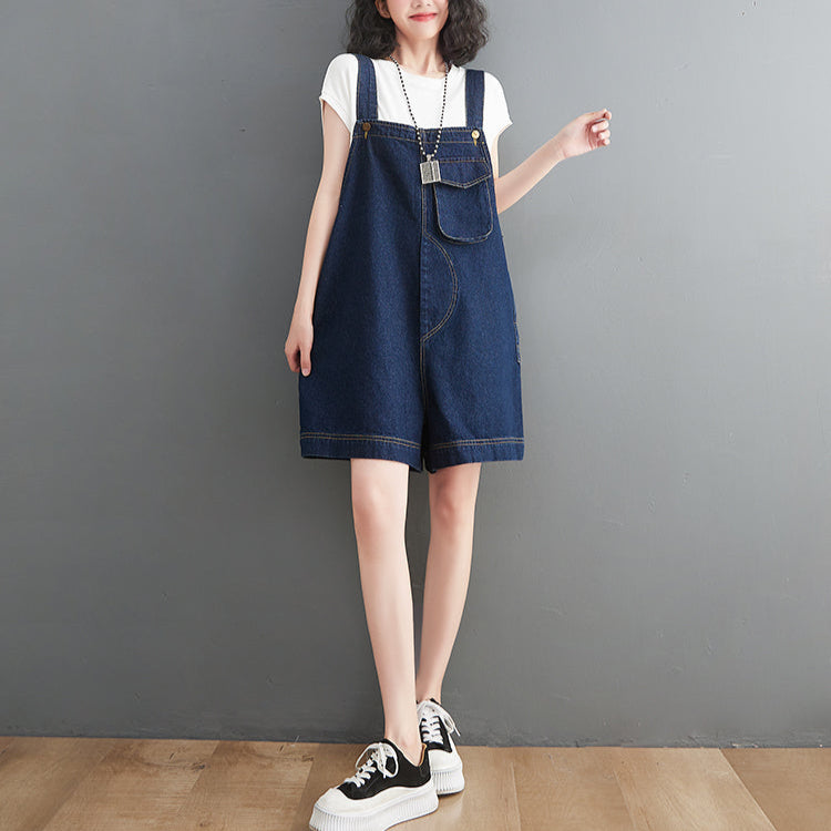 Person wearing a blue denim shortalls over a white shirt against a gray background