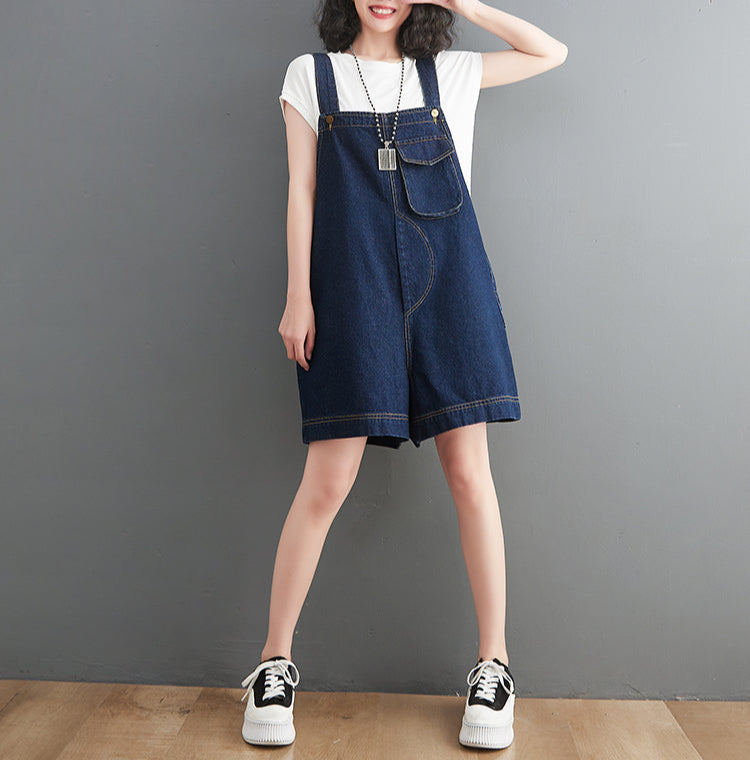 Person wearing a denim overalls dress against a gray background