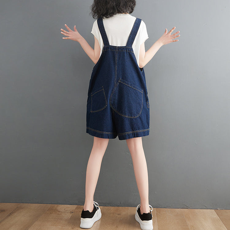 Person wearing a denim overall dress against a gray background