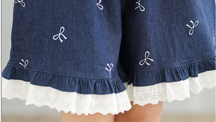 Blue denim shorts with white lace trim and embroidered bows on a neutral background
