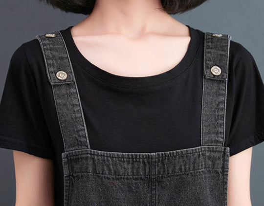 Person wearing a black t-shirt and denim overalls with text on a dark background
