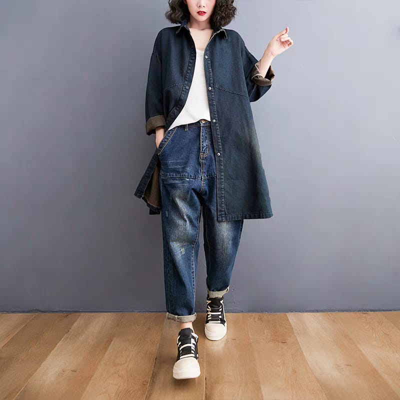 Person wearing a denim jacket and jeans standing against a gray wall.