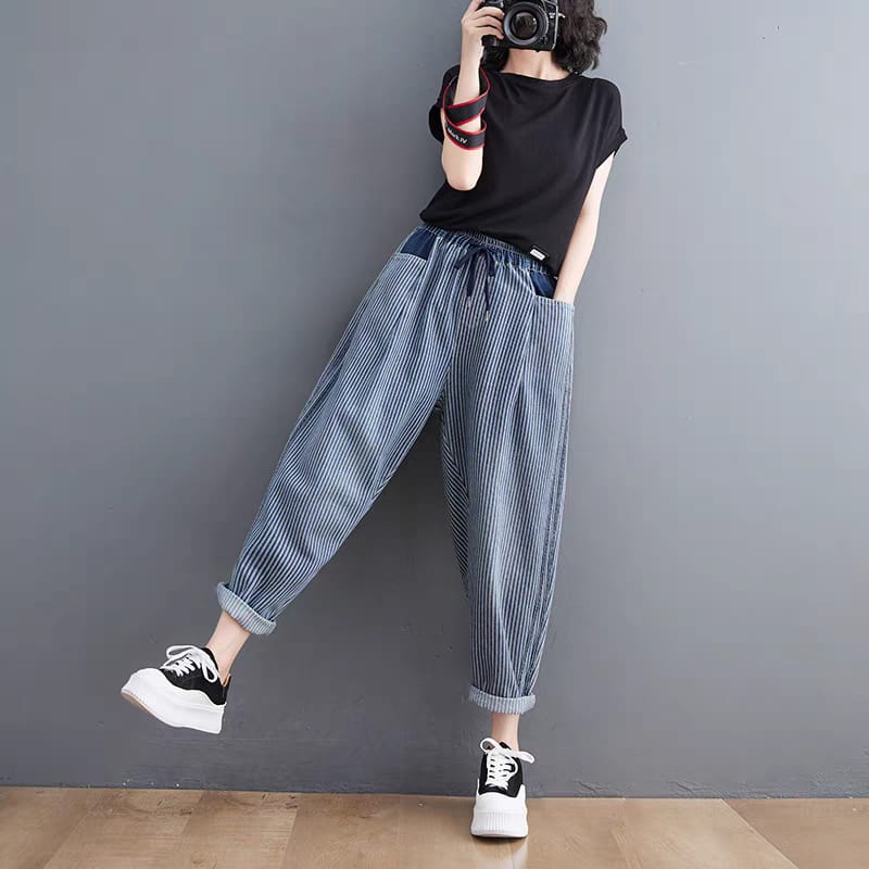 Person wearing blue striped harem pants and black sneakers against a gray wall.