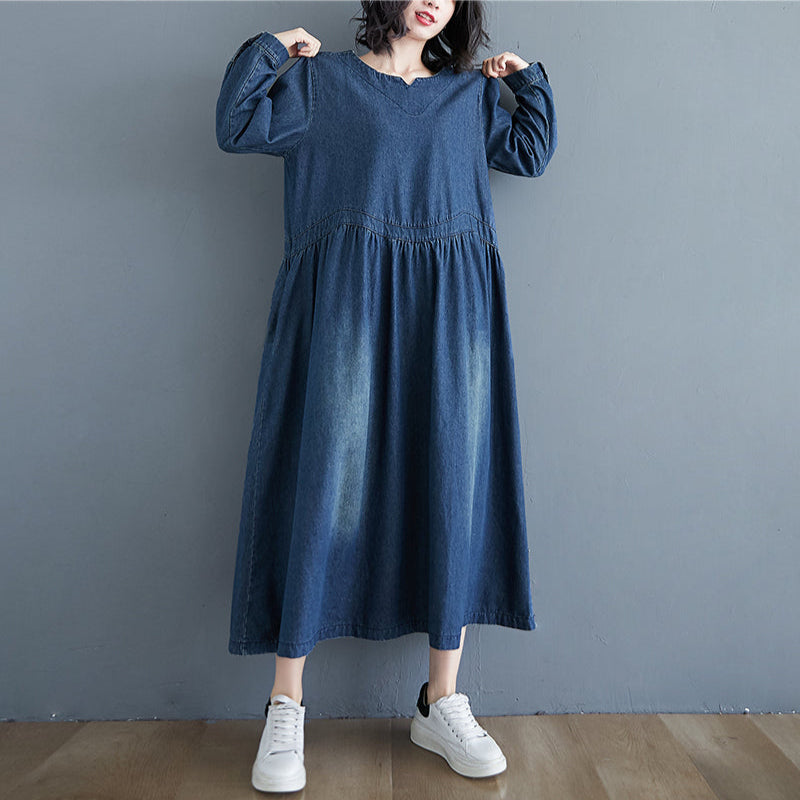Person wearing a blue dress with long sleeves against a gray wall.