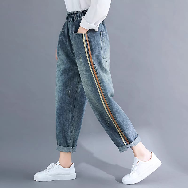 Person wearing blue jeans with side stripes and white sneakers on a gray background