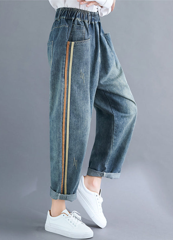Blue denim pants with a gold stripe worn by a person on a gray background