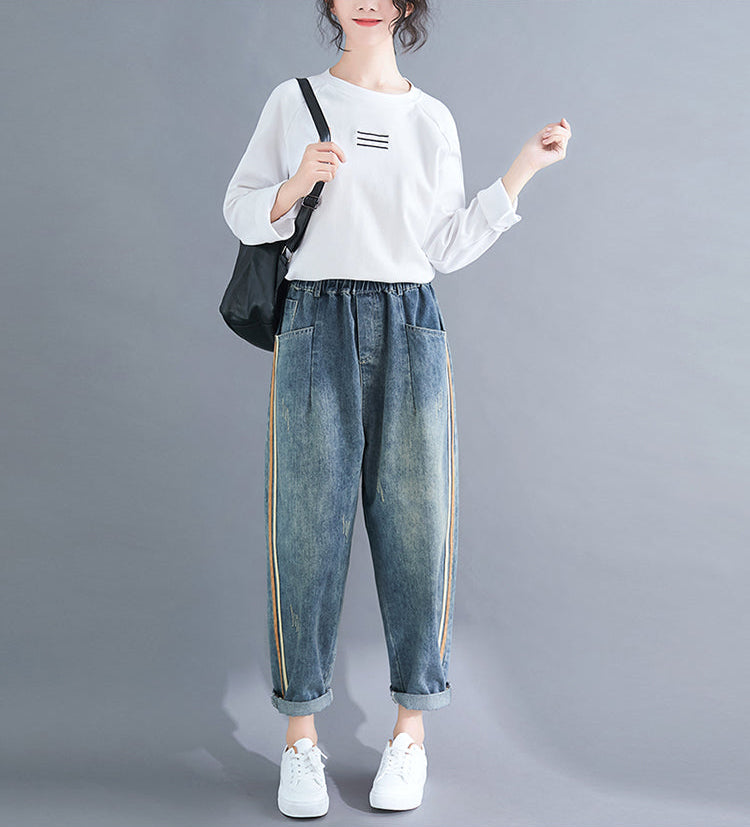 Person wearing a white sweater and blue jeans with yellow stripes on a gray background