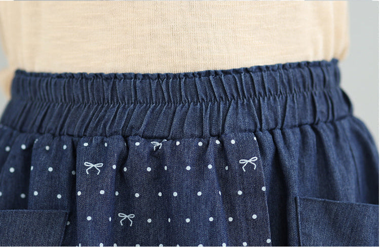 Close-up of a blue denim skirt with white polka dots and small patterns, worn over a beige top.