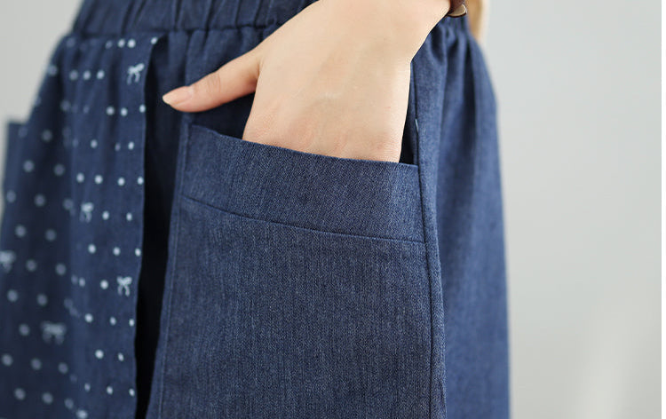 Close-up of a blue denim skirt with white polka dots and small patterns, worn over a beige top.