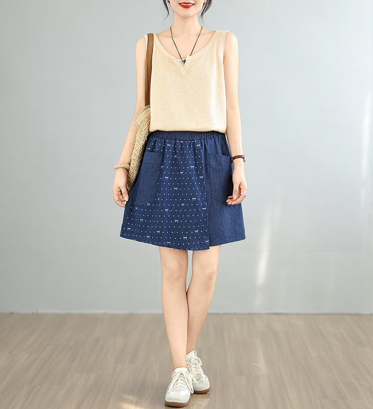 Woman wearing a beige top and blue polka dot skirt with white sneakers on a plain background