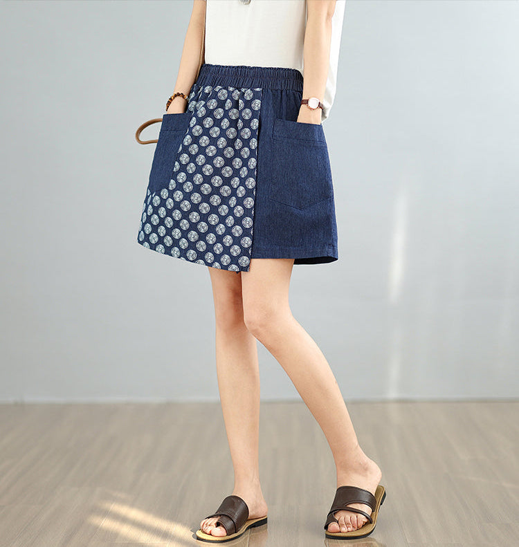 Person wearing a blue denim skirt with white floral pattern on a plain background