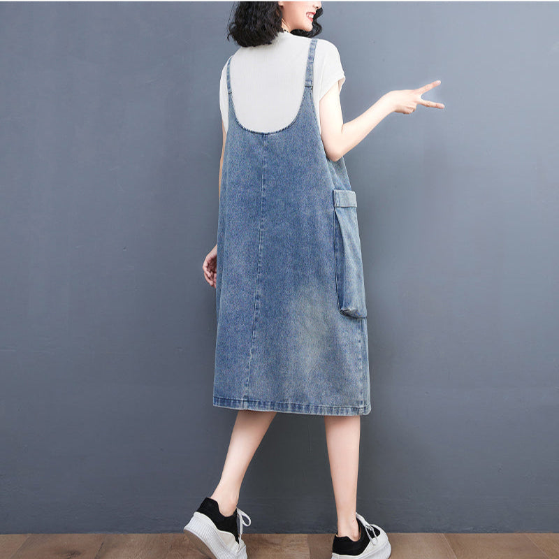 Person wearing a denim pinafore dress against a gray background