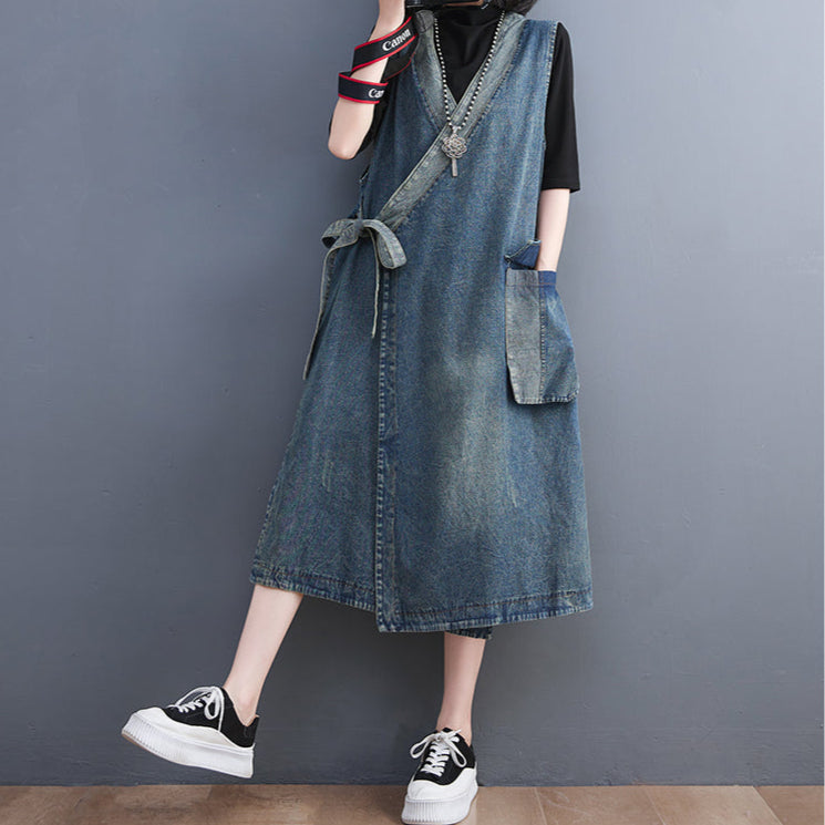 Person wearing a denim dress with suspenders against a plain background