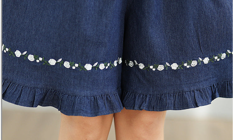 Close-up of a blue denim skirt with floral embroidery on a neutral background