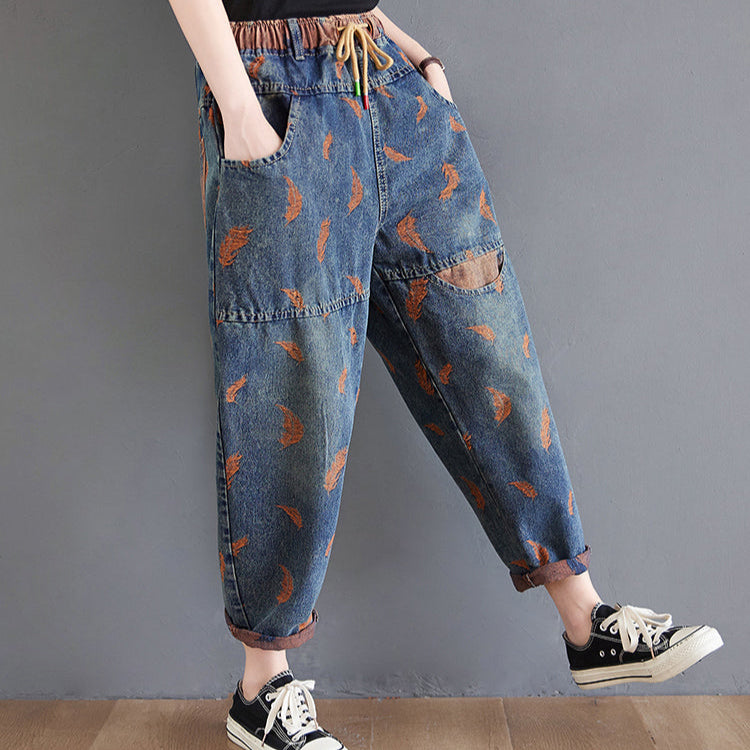 Person wearing blue denim pants with brown patterns and black sneakers on a gray background