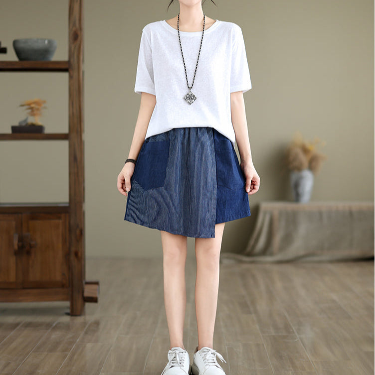 Woman wearing a white top and blue skirt in a room with wooden floor and furniture.