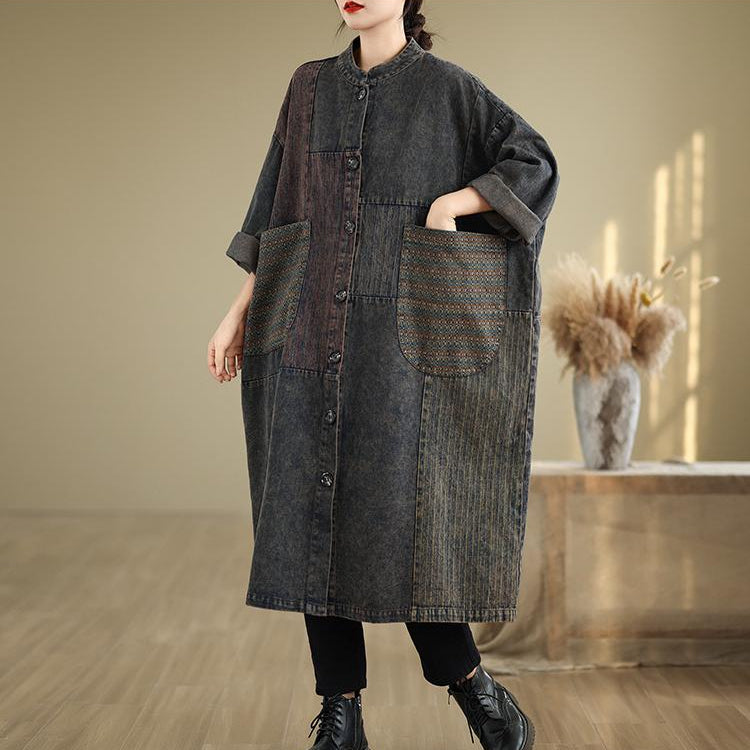 Person wearing a long dark denim coat in a minimalistic room.