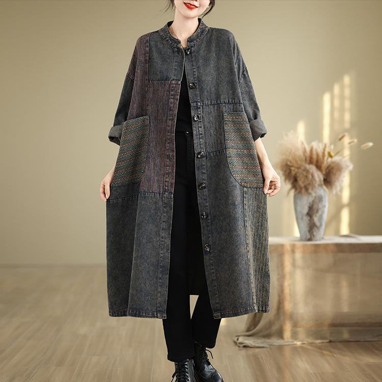 Person wearing a long dark denim jacket in a room with wooden floor and neutral wall.