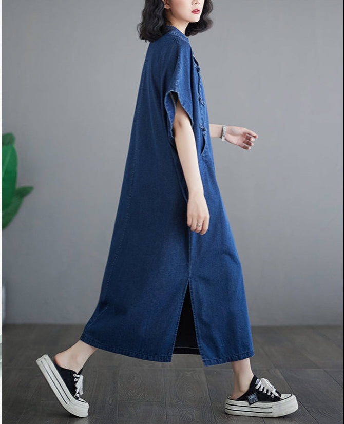 Person wearing a long blue denim dress with black sneakers on a gray background