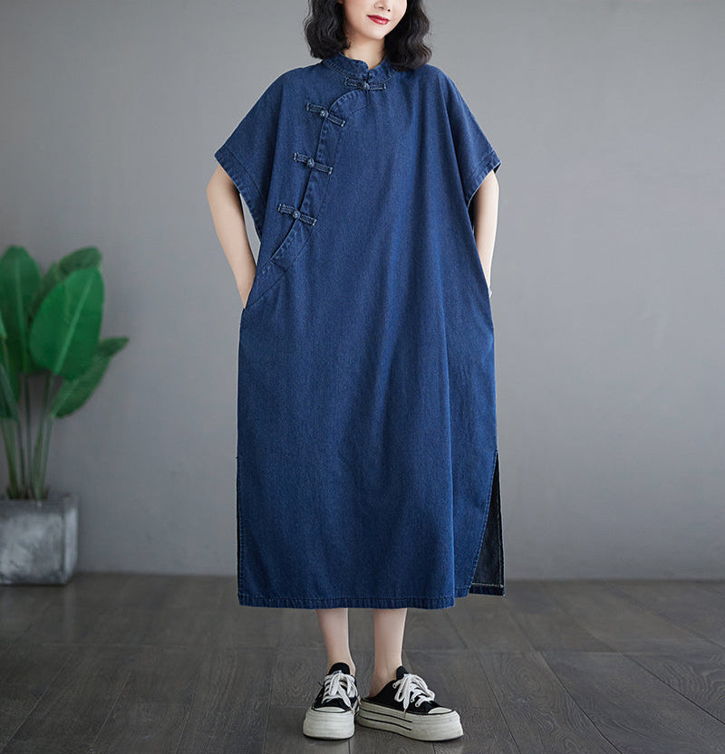 Person wearing a blue dress standing against a gray wall with a plant in the background