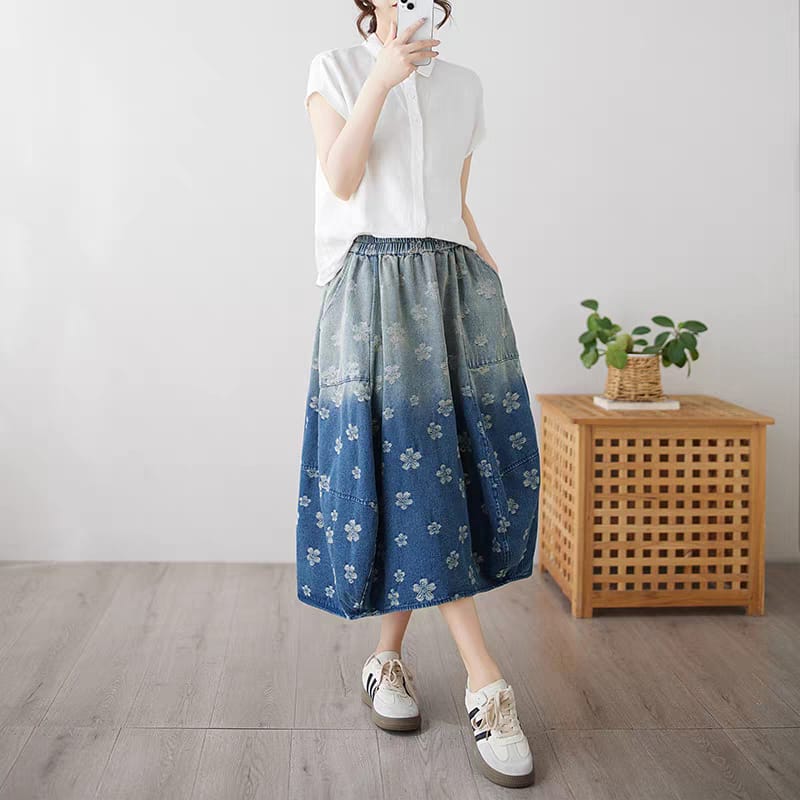 Person wearing a white shirt and blue floral skirt in a minimalistic room.
