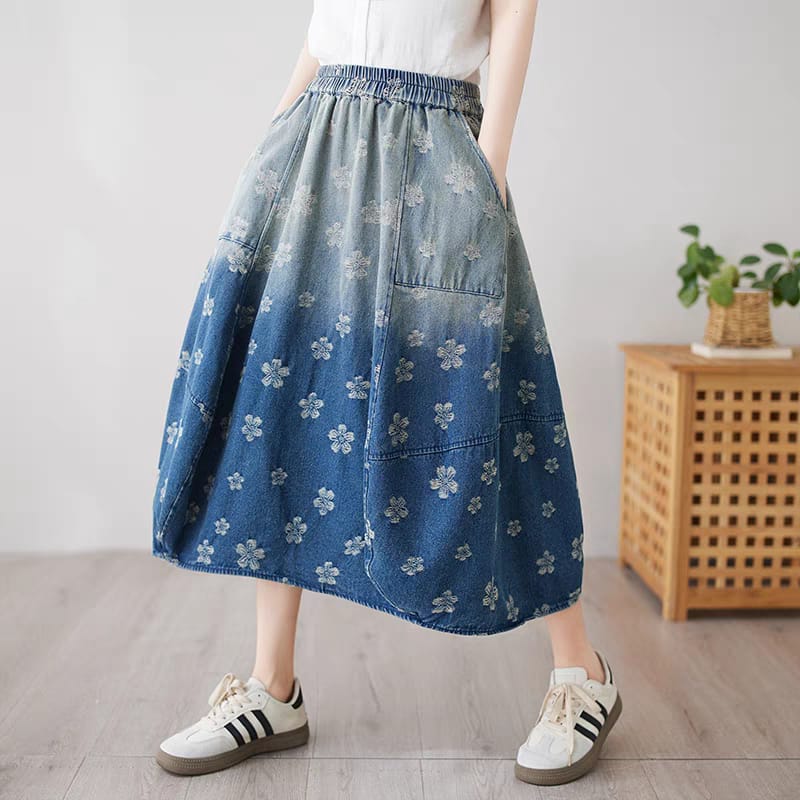 Person wearing a blue floral-patterned denim skirt with white sneakers in a minimal indoor setting.