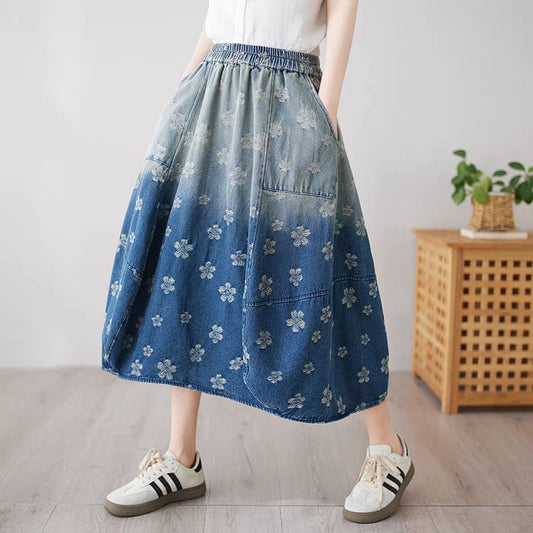Person wearing a blue floral-patterned denim skirt with white sneakers in a minimal indoor setting.