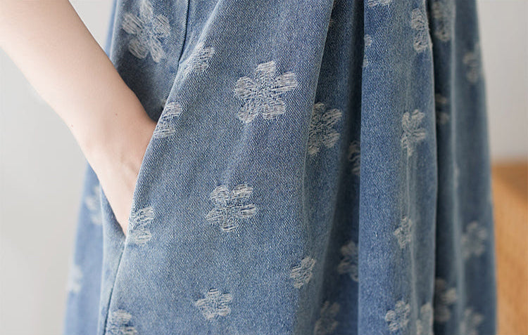 Blue floral-patterned denim pinafore dress over a white shirt on a plain background