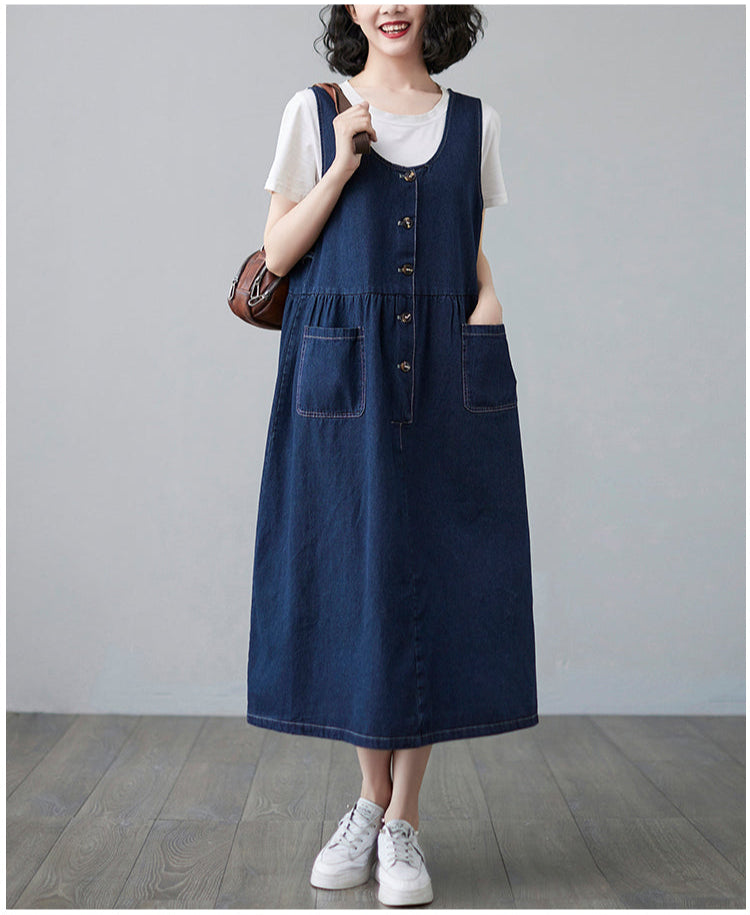 Woman wearing a blue denim dress over a white shirt with a brown bag against a gray background
