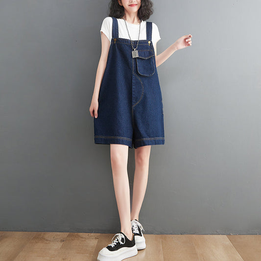 Person wearing a blue denim shortalls over a white shirt against a gray background