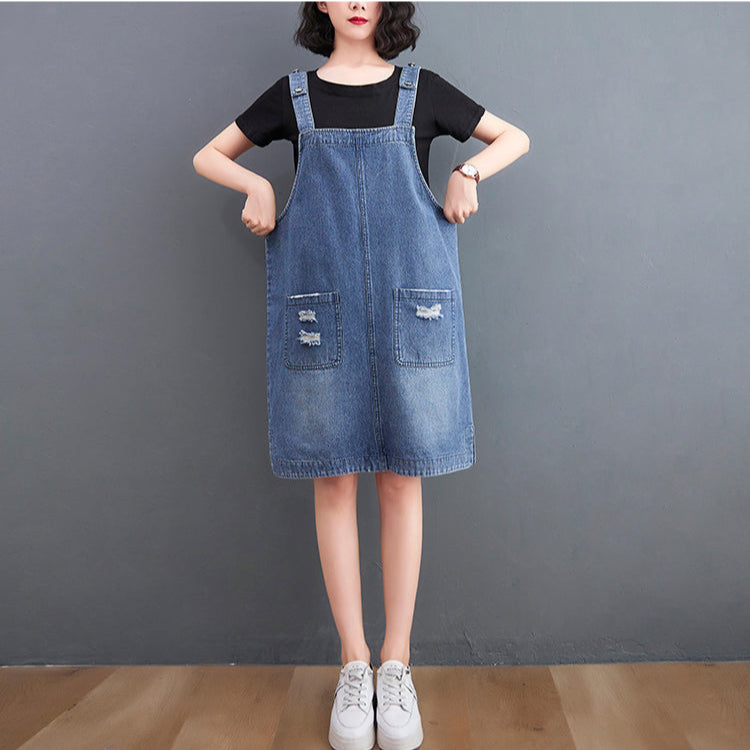 Person wearing a denim dress over a black shirt against a gray background