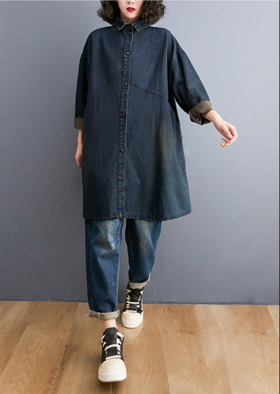 Person wearing a long denim dress with jeans and sneakers on a plain background