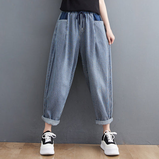 Person wearing a black top and blue striped pants against a gray wall.