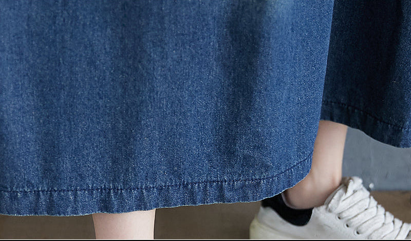 Close-up of a person wearing a blue denim skirt with white sneakers on a neutral background