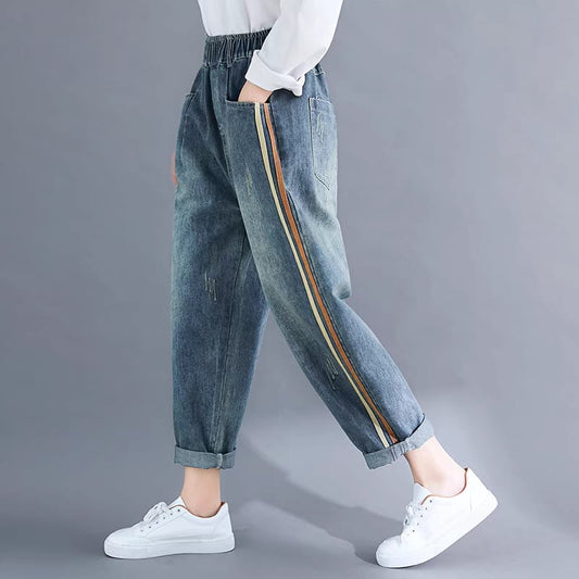 Person wearing blue jeans with side stripes and white sneakers on a gray background