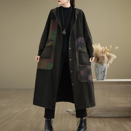 Person wearing a long dark coat with patterned patches in a minimalistic setting.