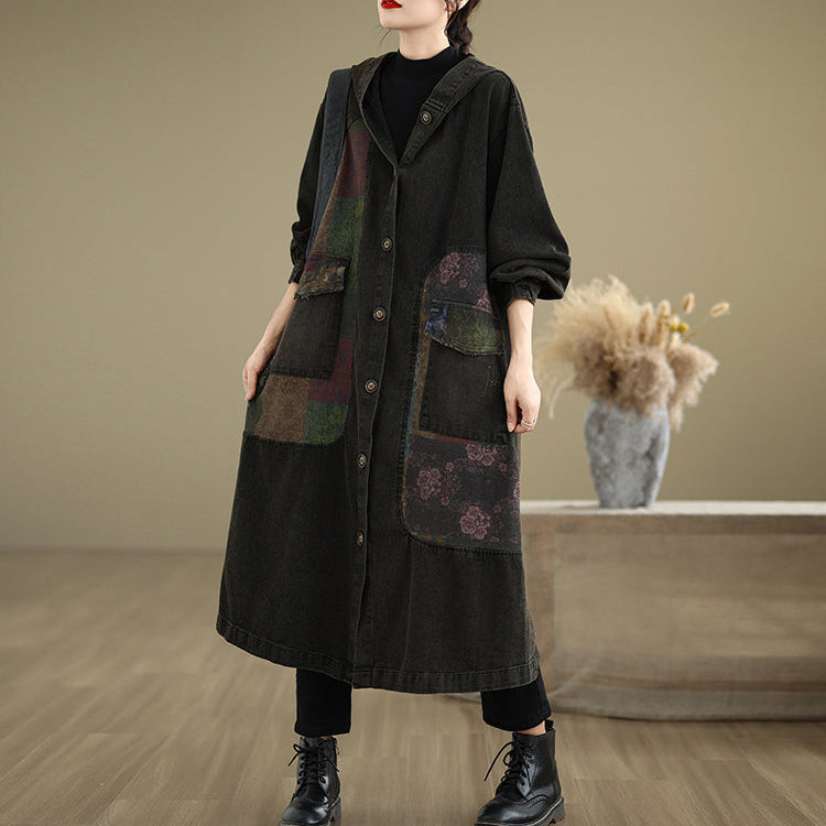 Person wearing a long black coat with floral patch details in a minimalistic setting.