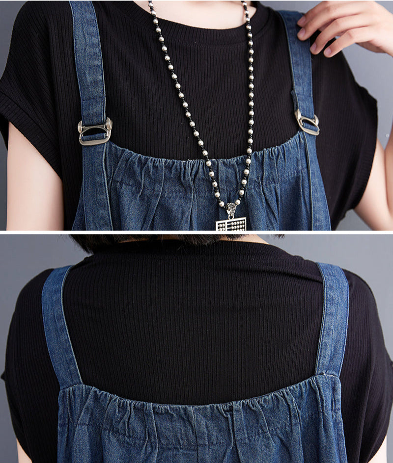 Person wearing a black top and blue denim overalls with a necklace.