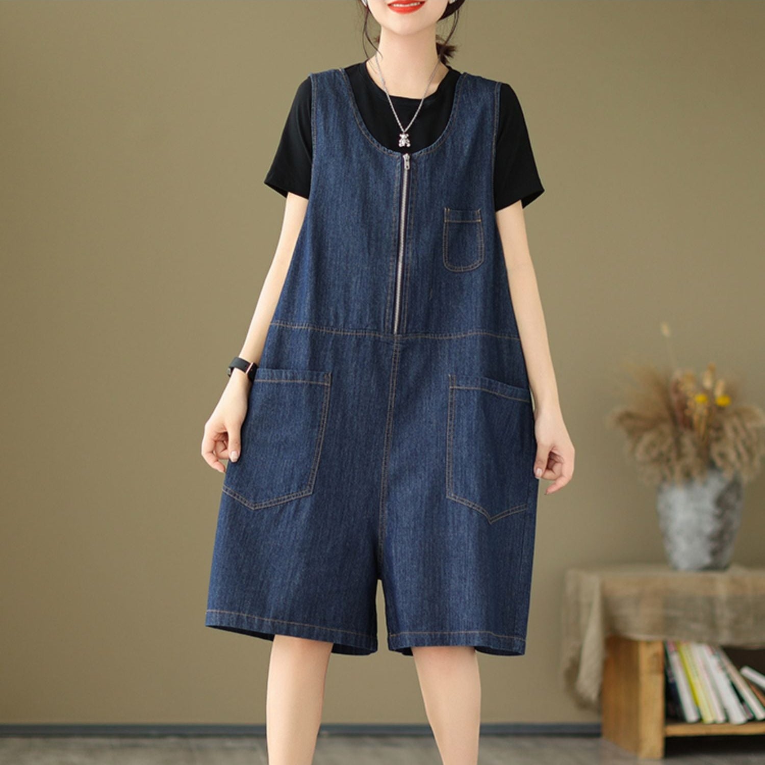 Woman wearing a denim dress over a black top in a room with a brown wall and wooden table.