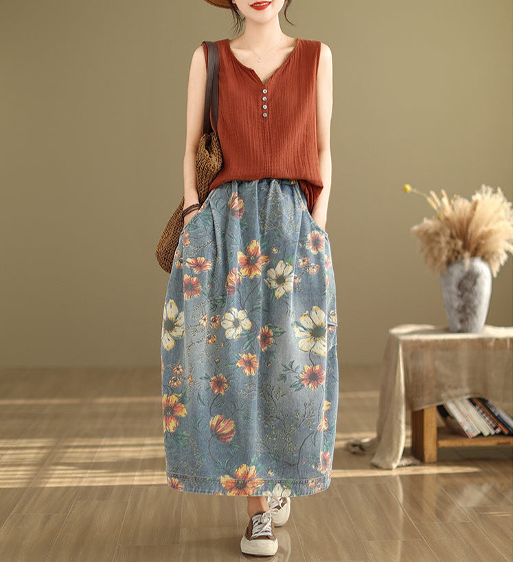 Woman wearing a rust-colored top and floral denim skirt in a room with a wooden floor and beige wall.
