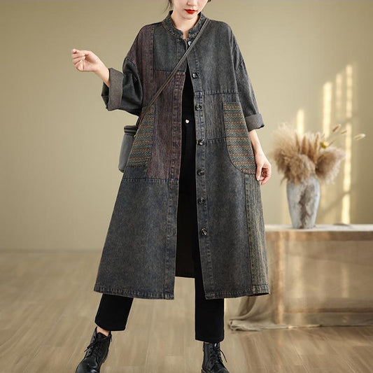Person wearing a long dark denim coat in an indoor setting with a neutral background